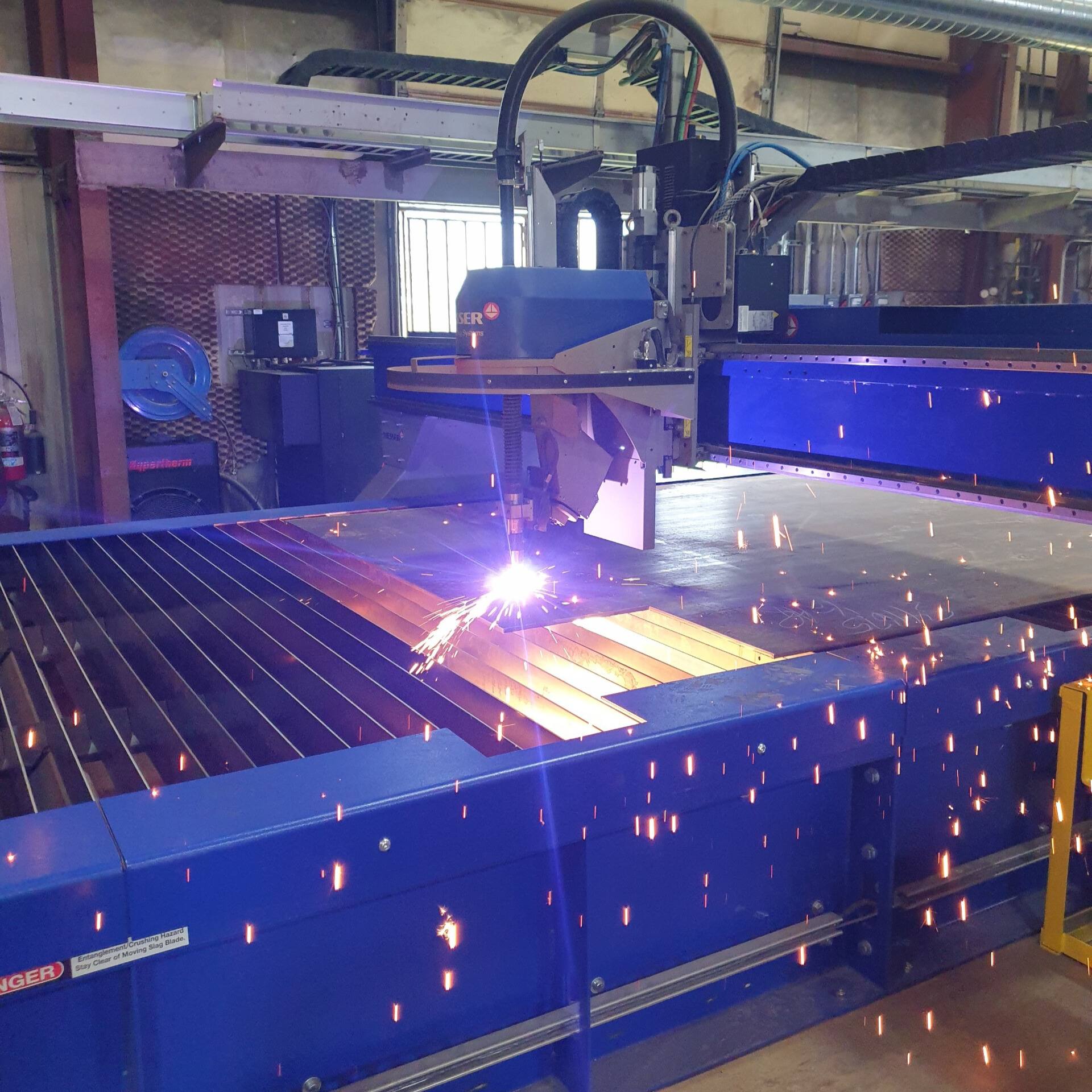 Plasma cutting table cutting steel plate with sparks flying in the PMI shop
