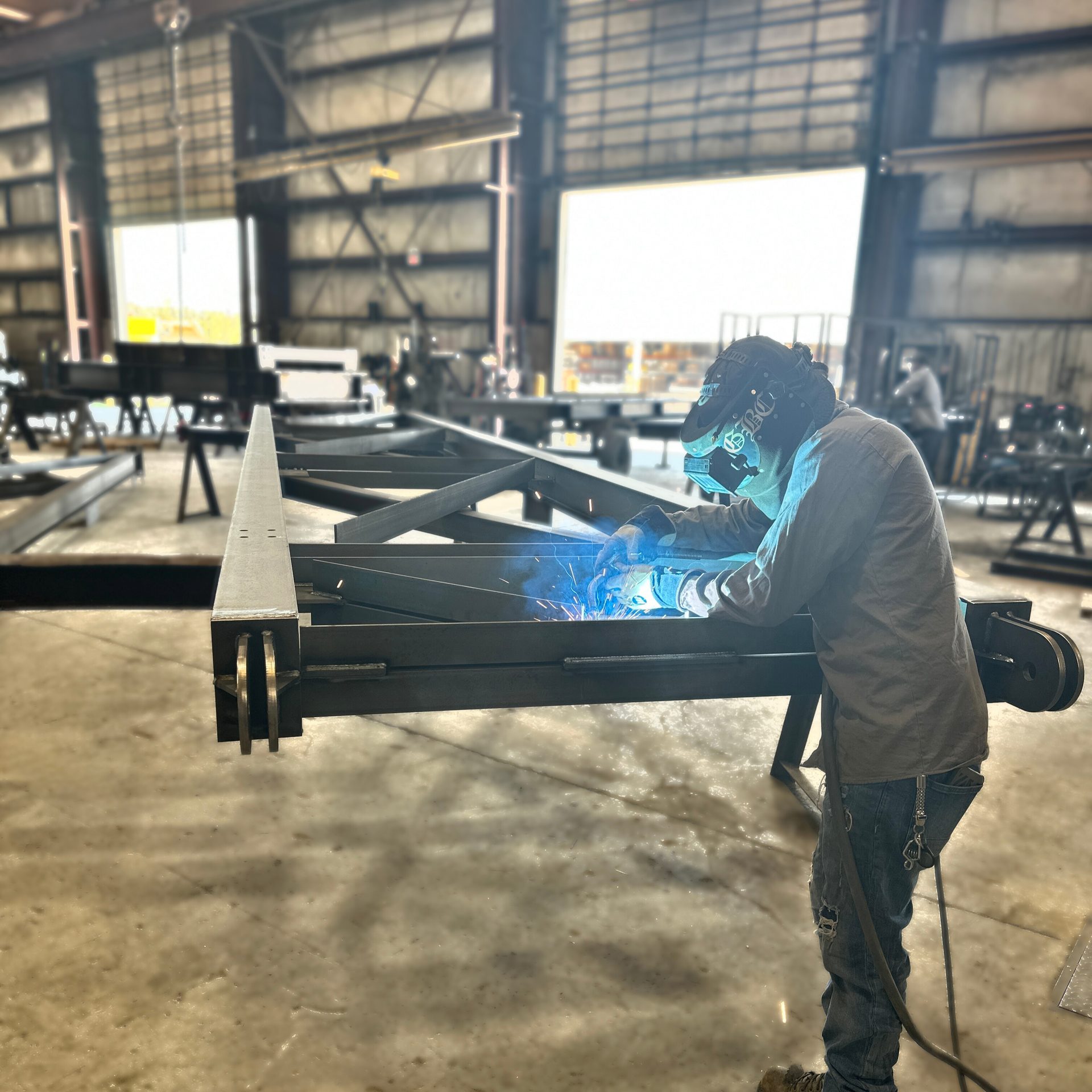 Welder in a welding helmet welding a steel truss section in a large fabrication shop